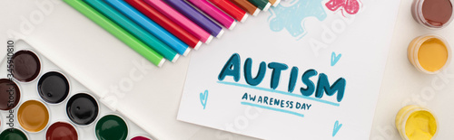 panoramic shot of card with Autism Awareness Day lettering and painting of puzzle on white with markers and paints