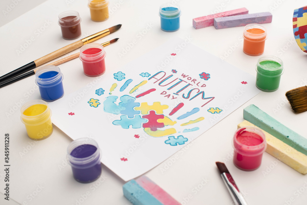 card with World Autism Day lettering and painting of puzzle and hand prints on white with paint brushes, chalks and paints card with World Autism Day lettering and painting of puzzle and hand prints on white with paint brushes, chalks and paints