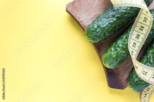 Fresh green cucumbers and yellow measuring tape on a yellow background, place for text.