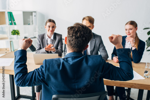 Selective focus of employee showing yes gesture near smiling recruiters in office