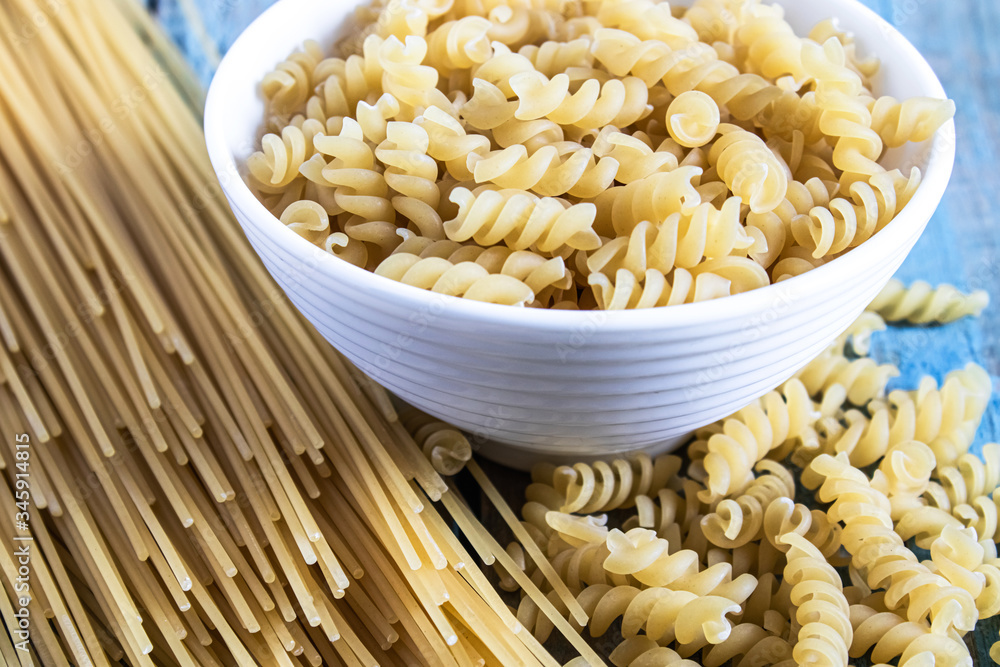 Dry pasta in a bowl on a background of blue boards near a pile of different pasta. Dry pasta in a bowl on a background of blue boards near a pile of different pasta.