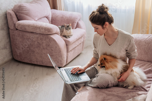the girl is working at the computer sitting on the sofa. the girl has a dog in her hands