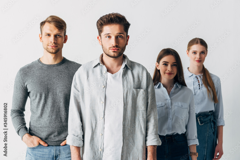 Selective focus of young man looking at camera near coworkers in office