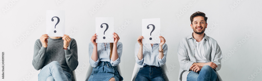 Panoramic shot of smiling man looking at camera near employees holding cards with question marks Panoramic shot of smiling man looking at camera near employees holding cards with question marks