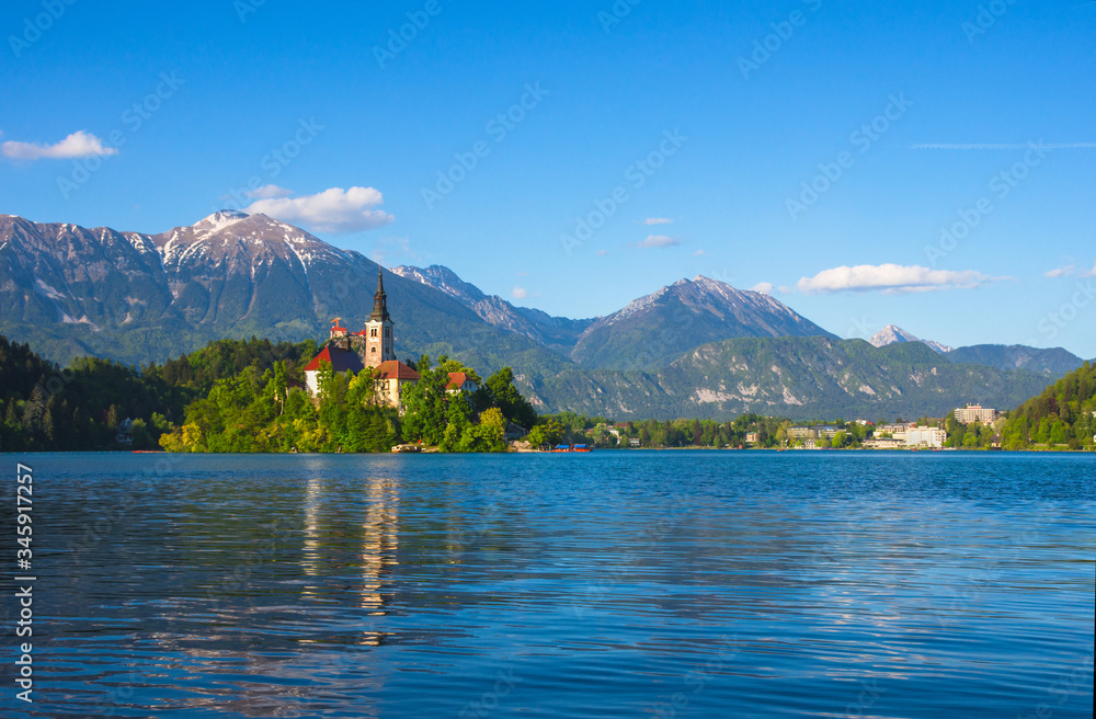 Sunny morning at Lake Bled and Julian Alps in the background. The lake island and charming little church dedicated to the Assumption of Mary are famous tourist attraction in Slovenia