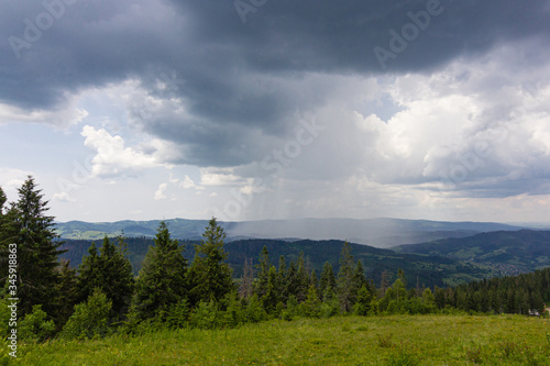 Shower rain and dark stormy clouds ove green summer Carpathian mountains