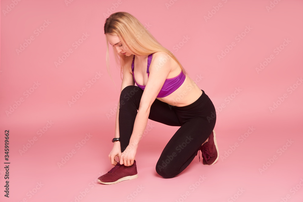 Girl lacing shoes getting ready for workout, pink background Girl lacing shoes getting ready for workout, pink background