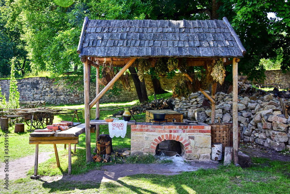 Cesis, Latvia - The medieval castle of Venden, a courtyard, a herbalist's shop an oven stands under a wooden canopy, next to the destroyed stone walls, green grass and trees.