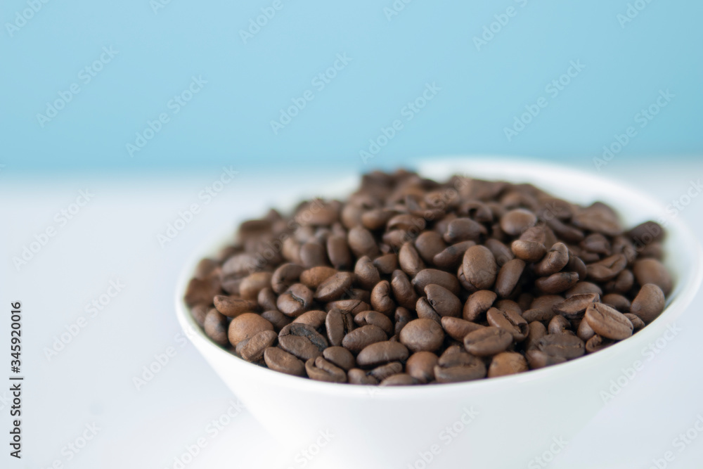 Fototapeta premium Roasted coffee beans in a white bowl with sky blue background