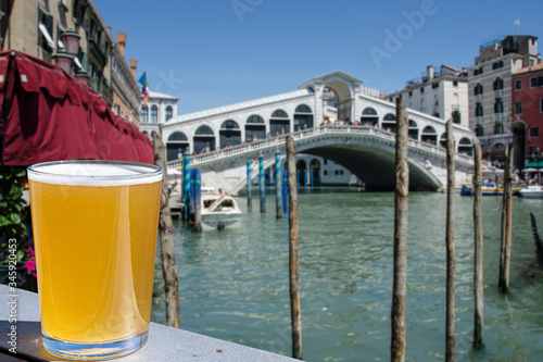 Glass of light beer with view on  famous Canal Grande and Rialto Bridge in Venice, Italy