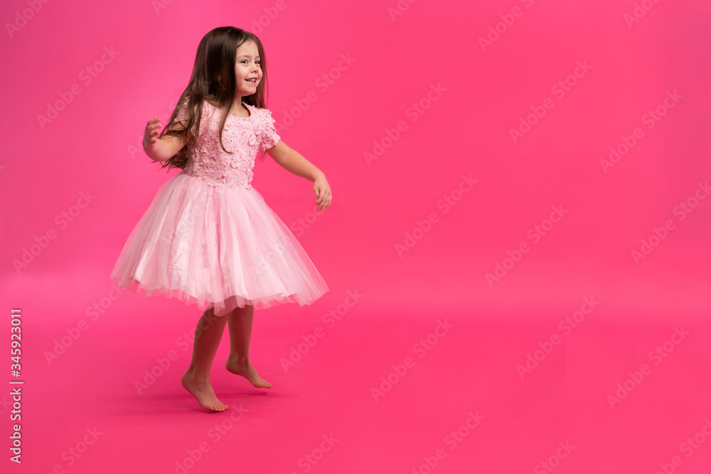 Cute little girl dreams of becoming a ballerina. Little Dancing Girl. Studio Shoot Over Pink Background