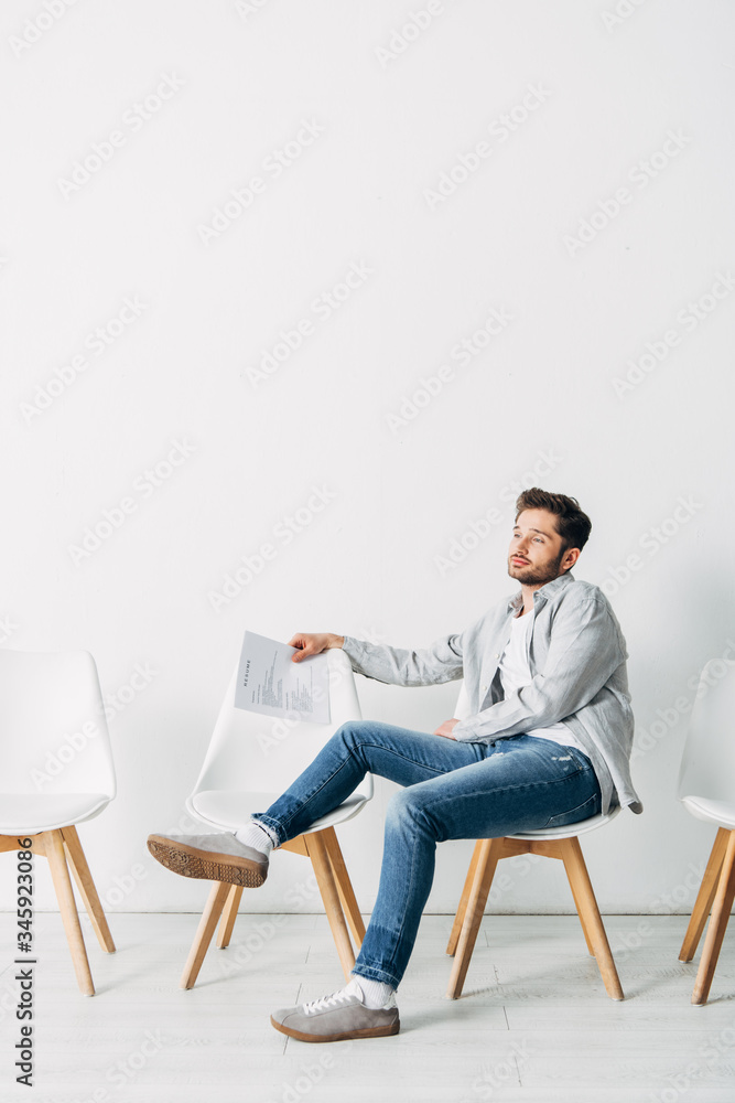 Handsome candidate with resume sitting on chair in office Handsome candidate with resume sitting on chair in office