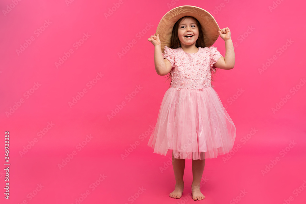Portrait of cute little girl in straw hat and pink dress in the studio on pink background. Copy space for text. Portrait of cute little girl in straw hat and pink dress in the studio on pink background. Copy space for text.