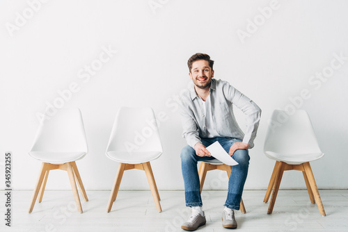 Smiling man with resume looking at camera while sitting on chair in office