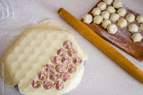 Traditional russian uncooked pelmeni on cutting board and ingredients for homemade pelmeni on white table. Process of making pelmeni, ravioli or dumplings with meat. Copy space. Side view.