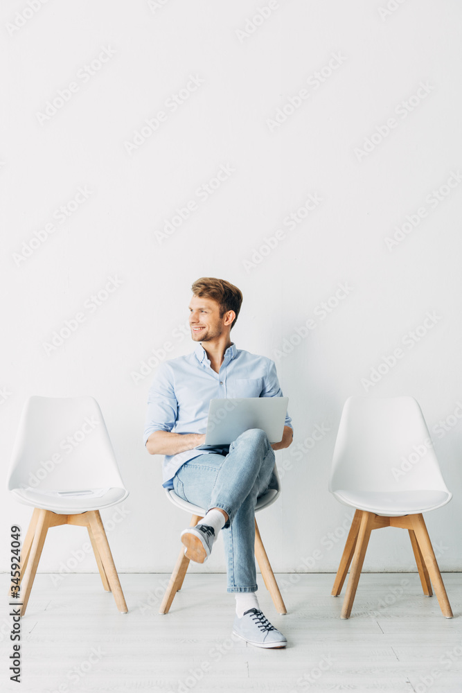 Fototapeta premium Smiling employee with laptop looking away in office