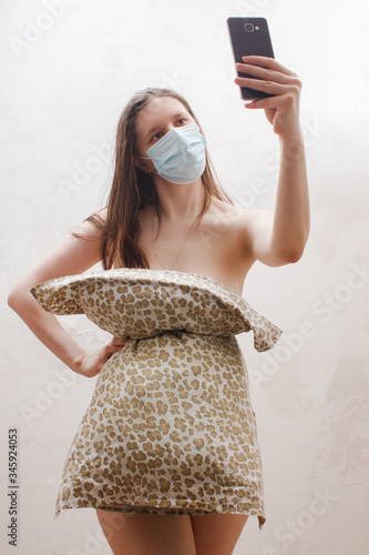 Woman in medical mask,  pillow dress making selfie photo on mobile phone for crazy Pillow Challenge due to stay home isolation. Fashion girl. Pillow Challenge due to home isolation.  photo