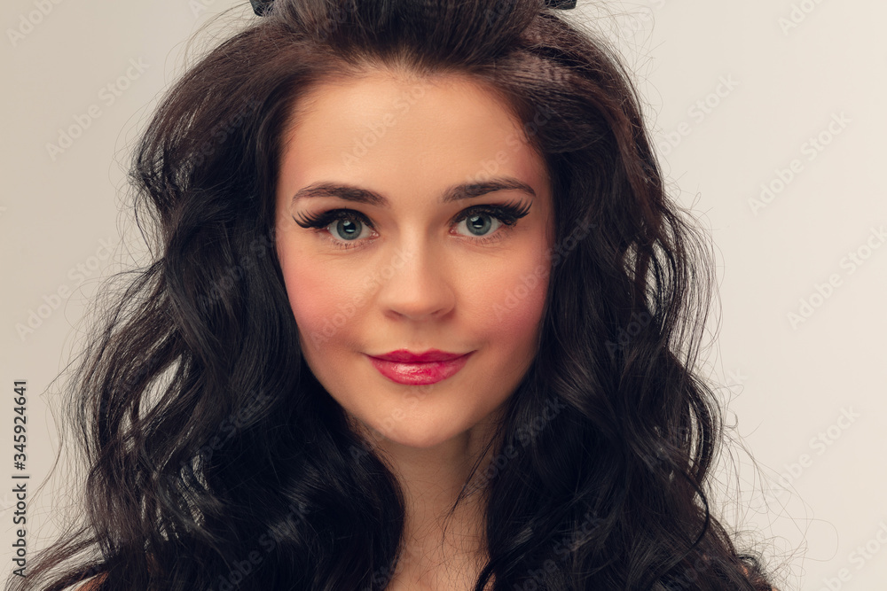 Naklejka premium Calm smiling. Portrait of beautiful young woman on grey studio background. Caucasian cute brunette female model with long curly hair. Concept of beauty, fashion, cosmetics. Copyspace for ad.