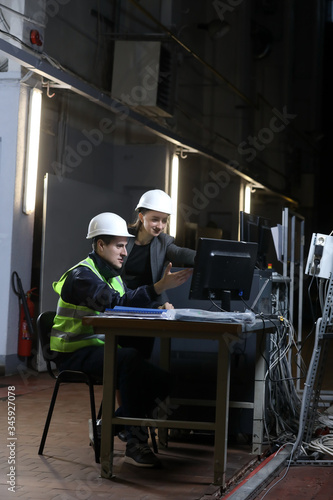 Portrait of a female factory manager in a white hard hat and business suit and factory engineer in work clothes. Controlling the work process in a factory.