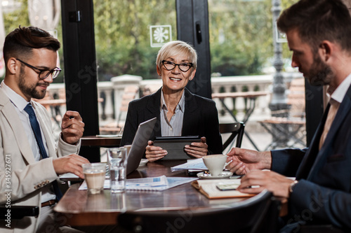 Portrait of senior businesswoman looking at camera while sitting in cafeteria with her colleagues.