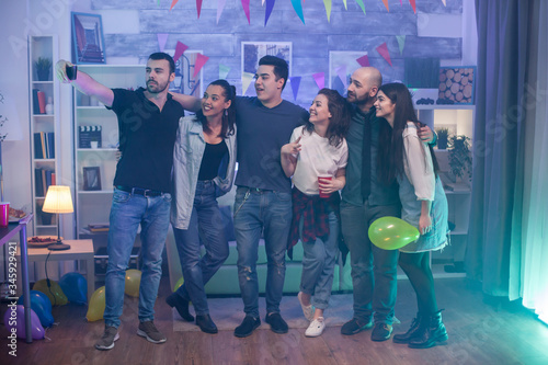 Group of young people taking a selfie at a party in an apartment..