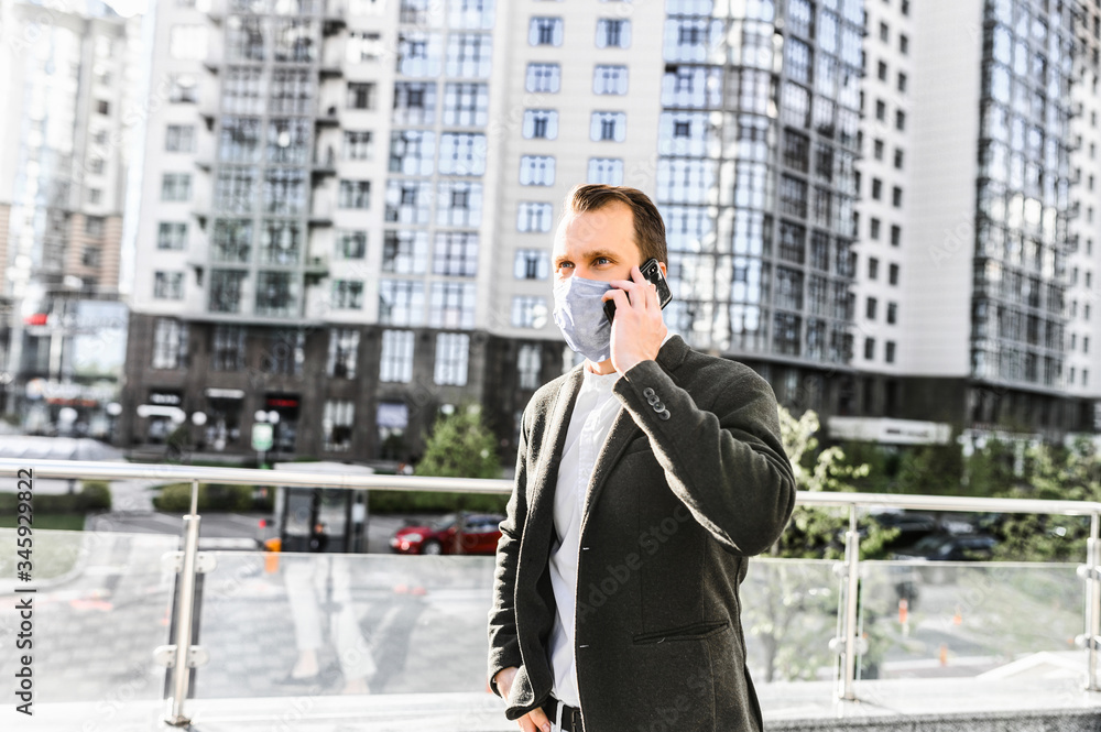 A guy in smart casual wear with a surgery protective mask on the face is talking on the phone in the downtown. Stay safety during quarantine, epidemia A guy in smart casual wear with a surgery protective mask on the face is talking on the phone in the downtown. Stay safety during quarantine, epidemia