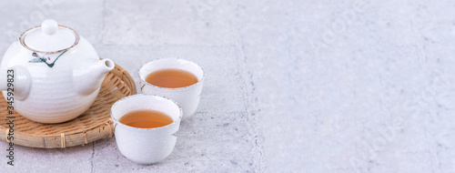 Hot tea in white teapot and cups on a sieve over bright gray cement background  closeup  copy space design concept.