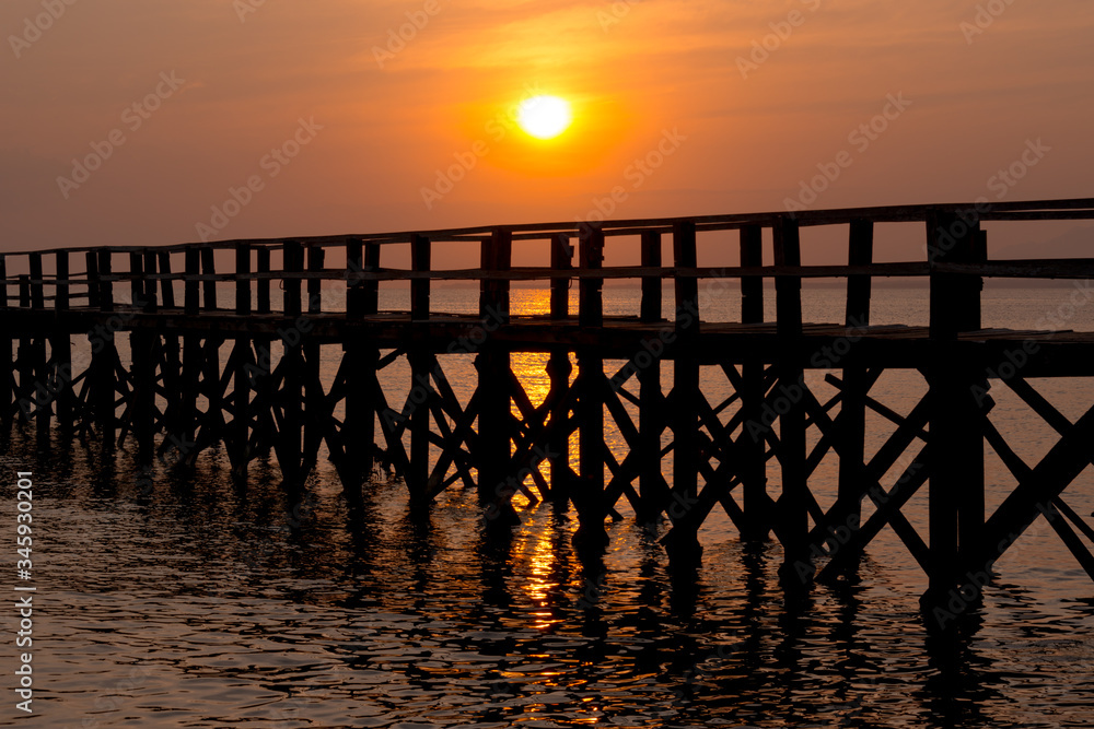 Sunset over the sea and a black wooden pier
