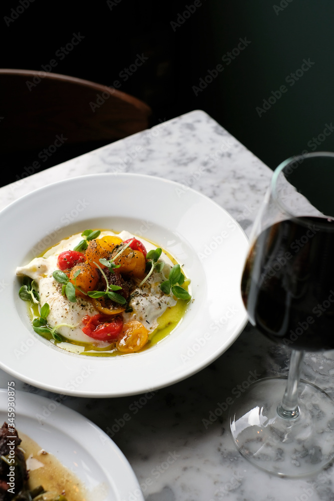 Classic Italian burrata and tomato salad is served in traditional restaurant with a glass of wine