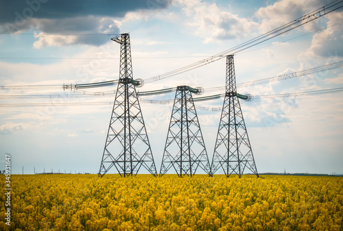 Transmission towers in the middle of a yellow canola field in bloom. High voltage power line at Spring
