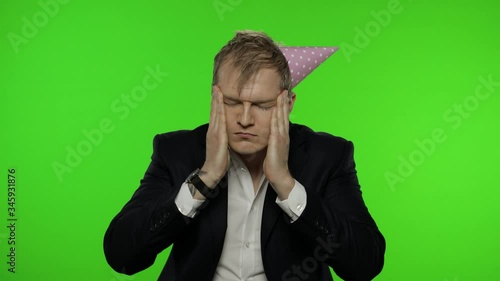 Drunk disheveled young businessman with hangover in festive cap having headache photo