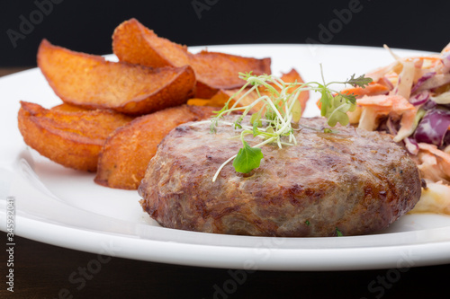 A burger with baked potatoes, cabbage and a salad in a ceramic plate on a wooden table