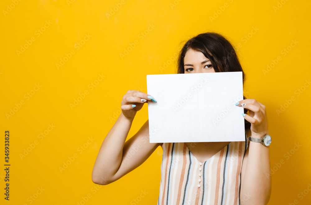 Image of young beautiful Asian girl smiling and holding a blank sheet of paper, isolated over yellow background Image of young beautiful Asian girl smiling and holding a blank sheet of paper, isolated over yellow background