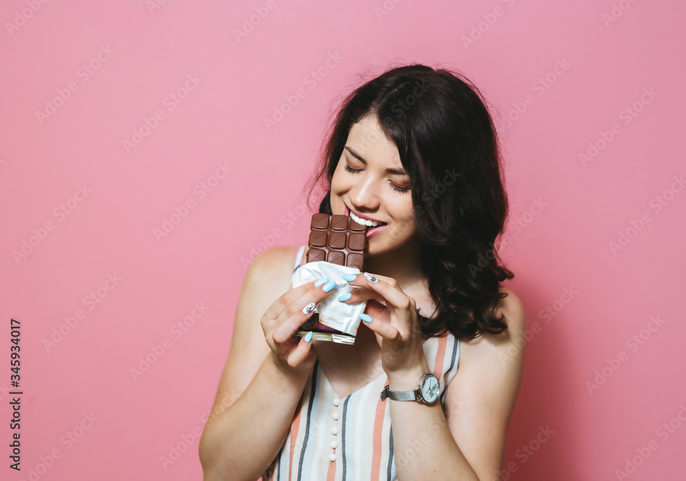 Image of happy cute Asian young woman standing isolated over pink background eating chocolate. Image of happy cute Asian young woman standing isolated over pink background eating chocolate.