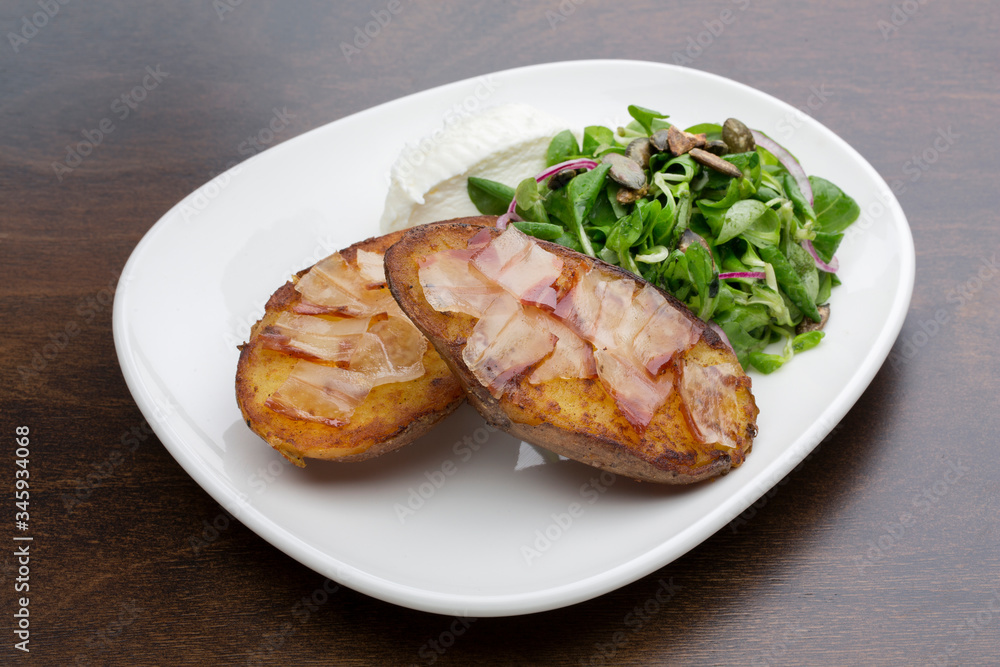 Baked potatoes with bacon, fresh cheese and a salad in a ceramic plate on a wooden table Baked potatoes with bacon, fresh cheese and a salad in a ceramic plate on a wooden table