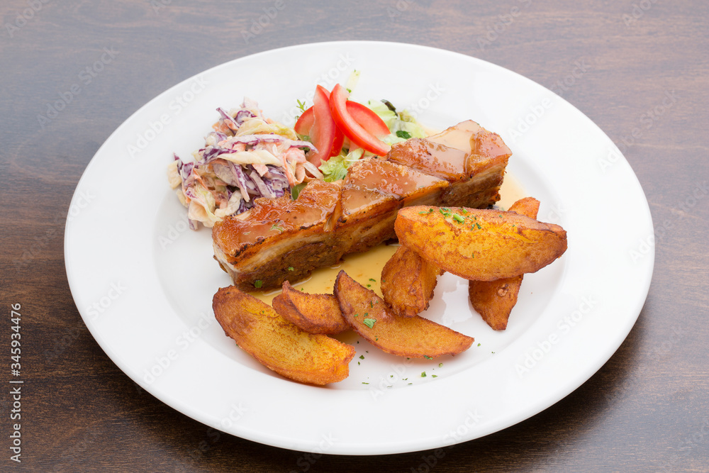 Pork ribs with roasted potatoes, cabbage and lettuce in a white ceramic plate on a wooden table