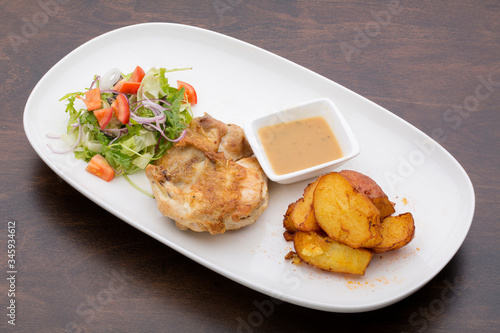 Roasted chicken with sauce, baked potatoes and a mixed salad in a white ceramic plate on a wooden table