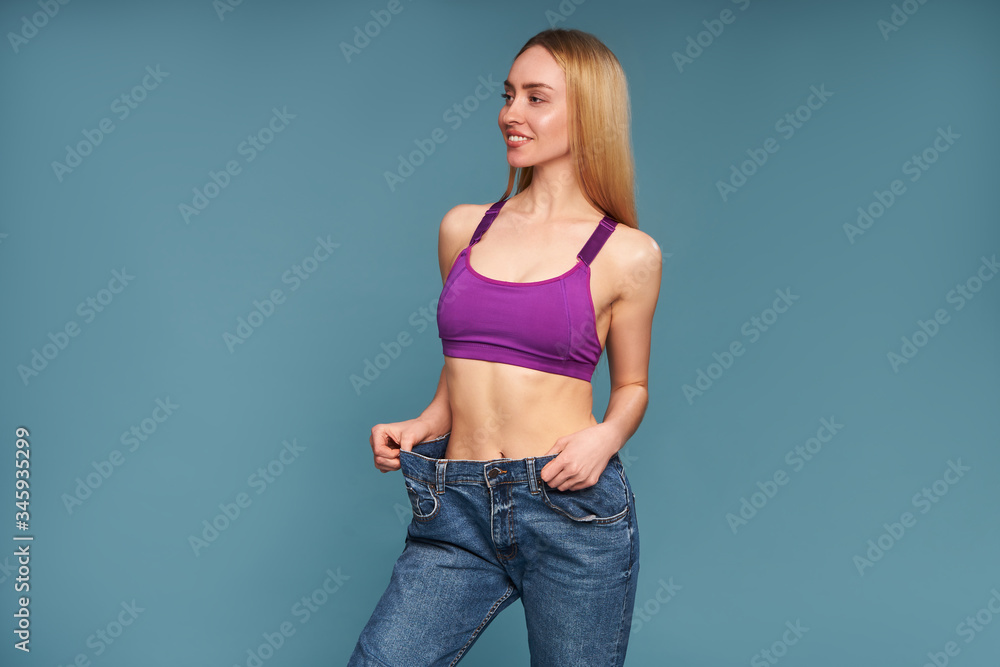Excited girl posing in oversized jeans on a blue studio background Excited girl posing in oversized jeans on a blue studio background