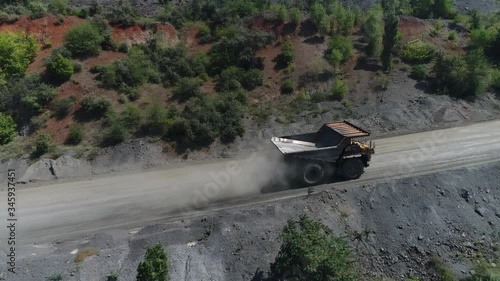 A huge mining dump truck is driving along the road of an iron ore quarry. View from a quadcopter