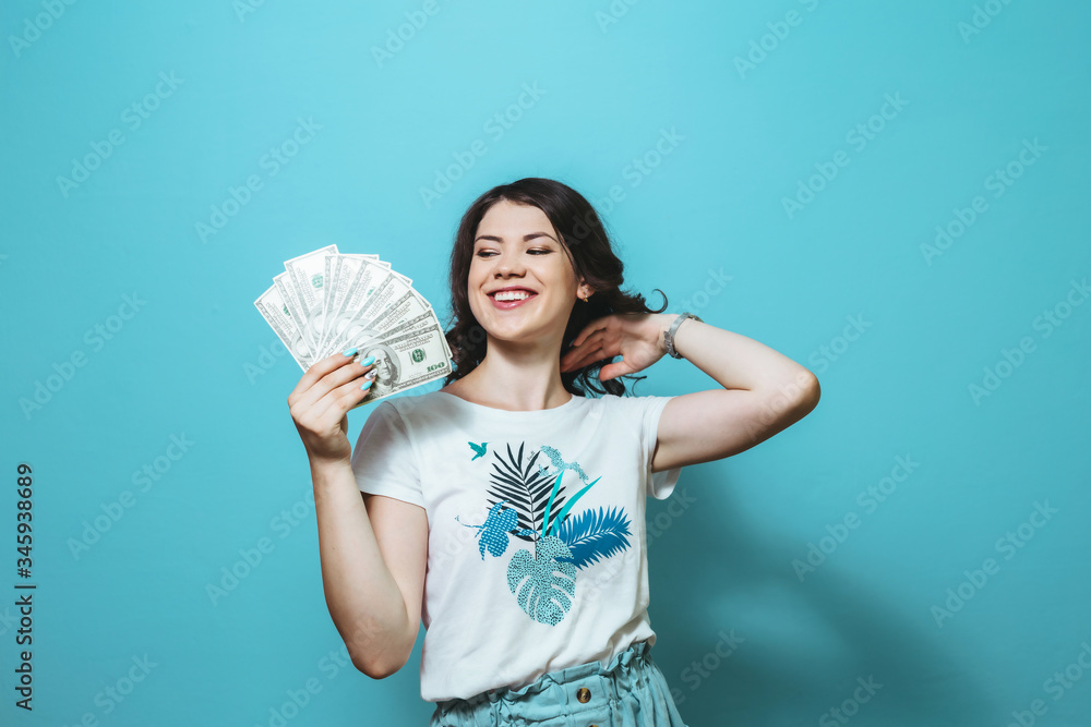 Portrait of a happy satisfied Asian girl holding bunch of money banknotes isolated over blue background Portrait of a happy satisfied Asian girl holding bunch of money banknotes isolated over blue background