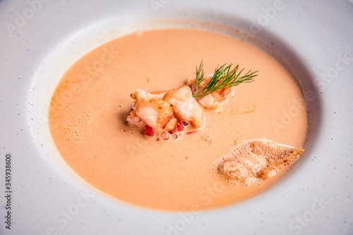 Closeup of creamy lobster bisque soup with grilled prawn and dill in white bowl