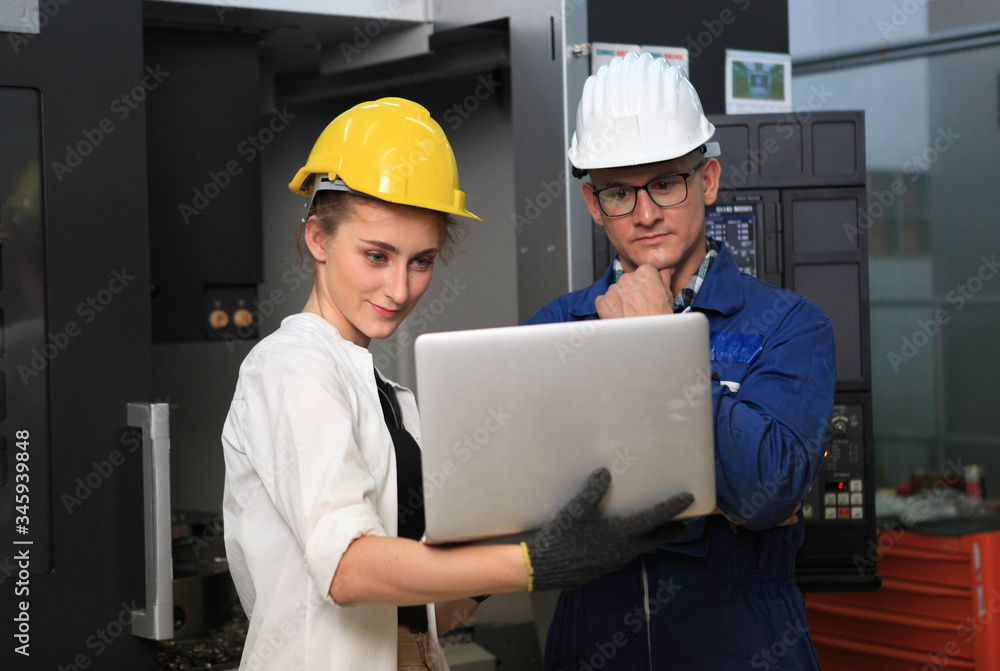 Male and Female Industrial Engineers in Hard Hats Discuss New Project while Using Laptop. They Work in a Heavy Industry Manufacturing Factory. Male and Female Industrial Engineers in Hard Hats Discuss New Project while Using Laptop. They Work in a Heavy Industry Manufacturing Factory.