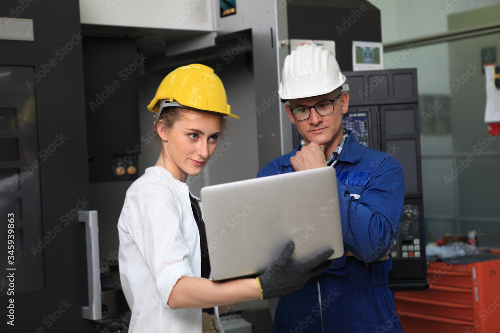 Male and Female Industrial Engineers in Hard Hats Discuss New Project while Using Laptop. They Work in a Heavy Industry Manufacturing Factory. Male and Female Industrial Engineers in Hard Hats Discuss New Project while Using Laptop. They Work in a Heavy Industry Manufacturing Factory.