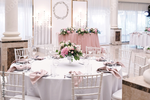 The luxurious round table for the wedding lunch is decorated with flowers and stylish dishes. Beautifully organized event - served festive tables ready for guests