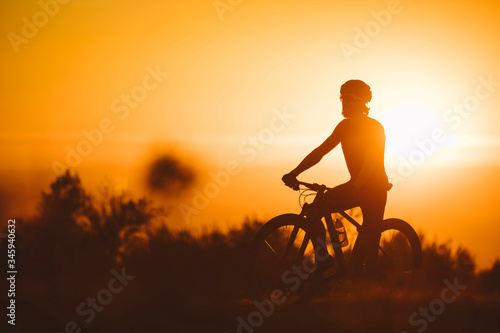 Silhouette of a cyclist man riding mountain bike on a mountain at sunset.