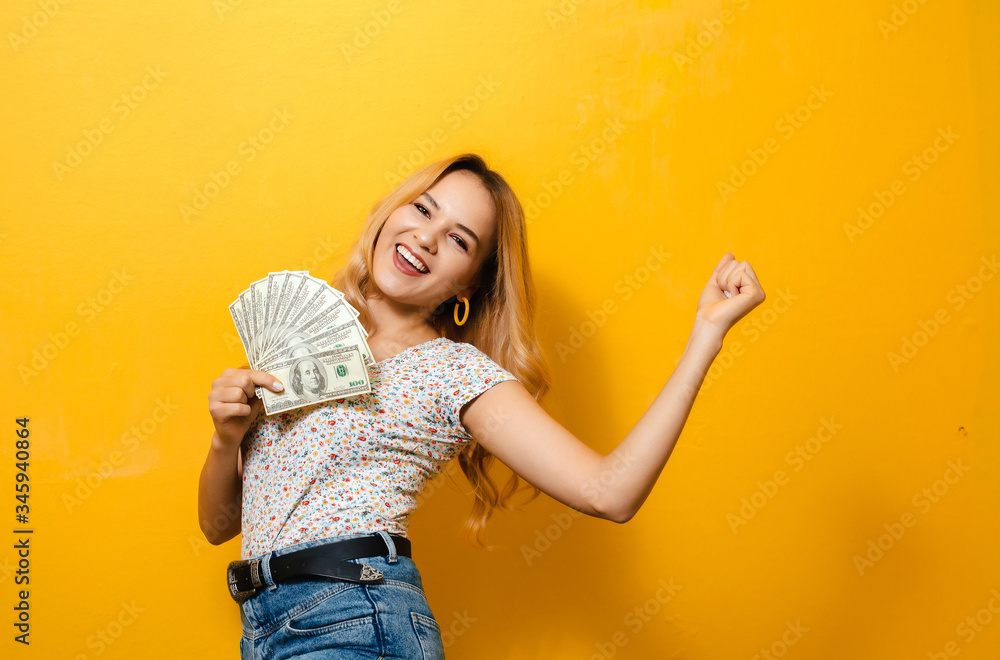 Portrait of a young blonde happy girl holding banknotes over yellow background Portrait of a young blonde happy girl holding banknotes over yellow background