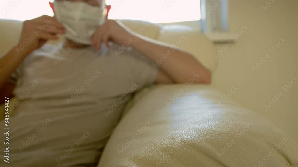 Self-isolation man out of focus sits on the couch and puts on a medical mask and leaves Self-isolation man out of focus sits on the couch and puts on a medical mask and leaves