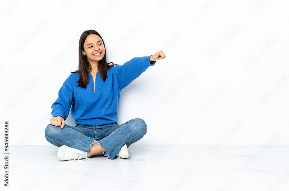 Young mixed race woman sitting on the floor isolated on white background giving a thumbs up gesture