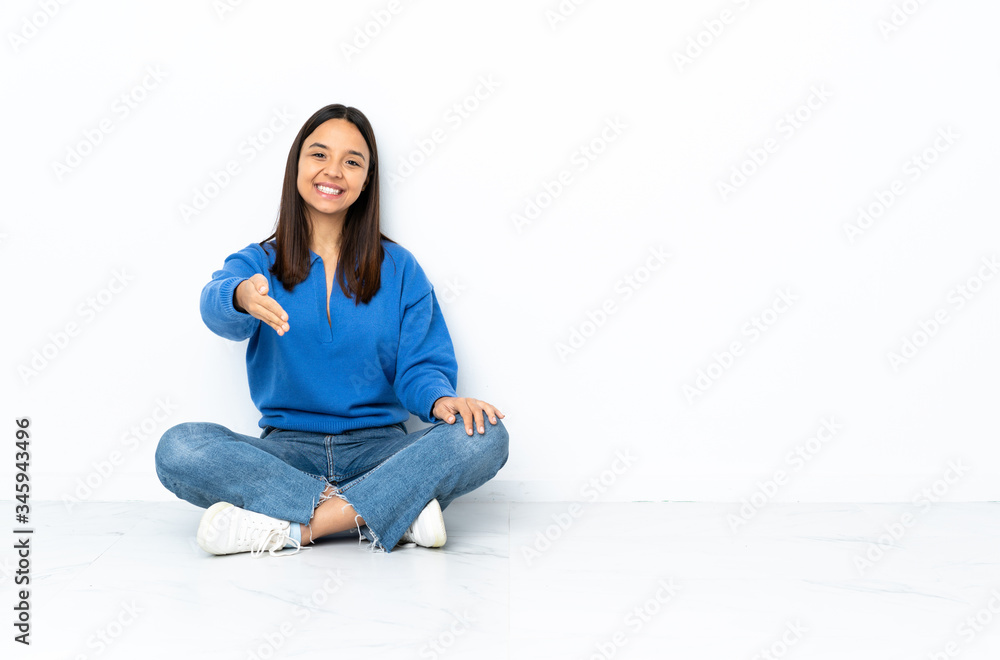 Young mixed race woman sitting on the floor isolated on white background shaking hands for closing a good deal Young mixed race woman sitting on the floor isolated on white background shaking hands for closing a good deal