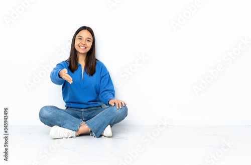 Young mixed race woman sitting on the floor isolated on white background shaking hands for closing a good deal